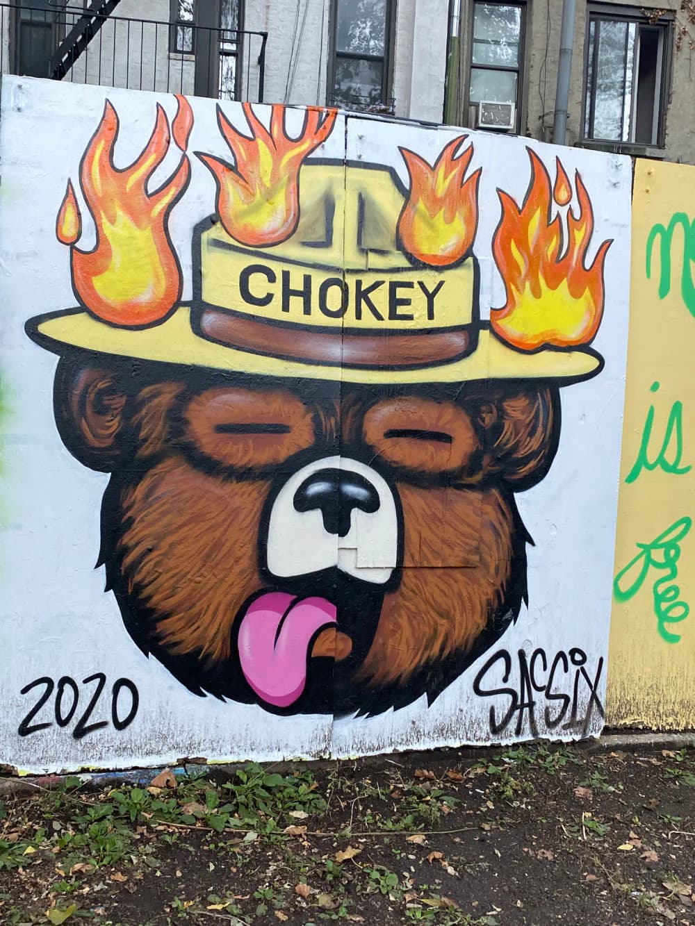 Colorful mural of brown bear wearing yellow hat with "CHOKEY" text surrounded by orange and yellow flames, tongue out, dated 2020.