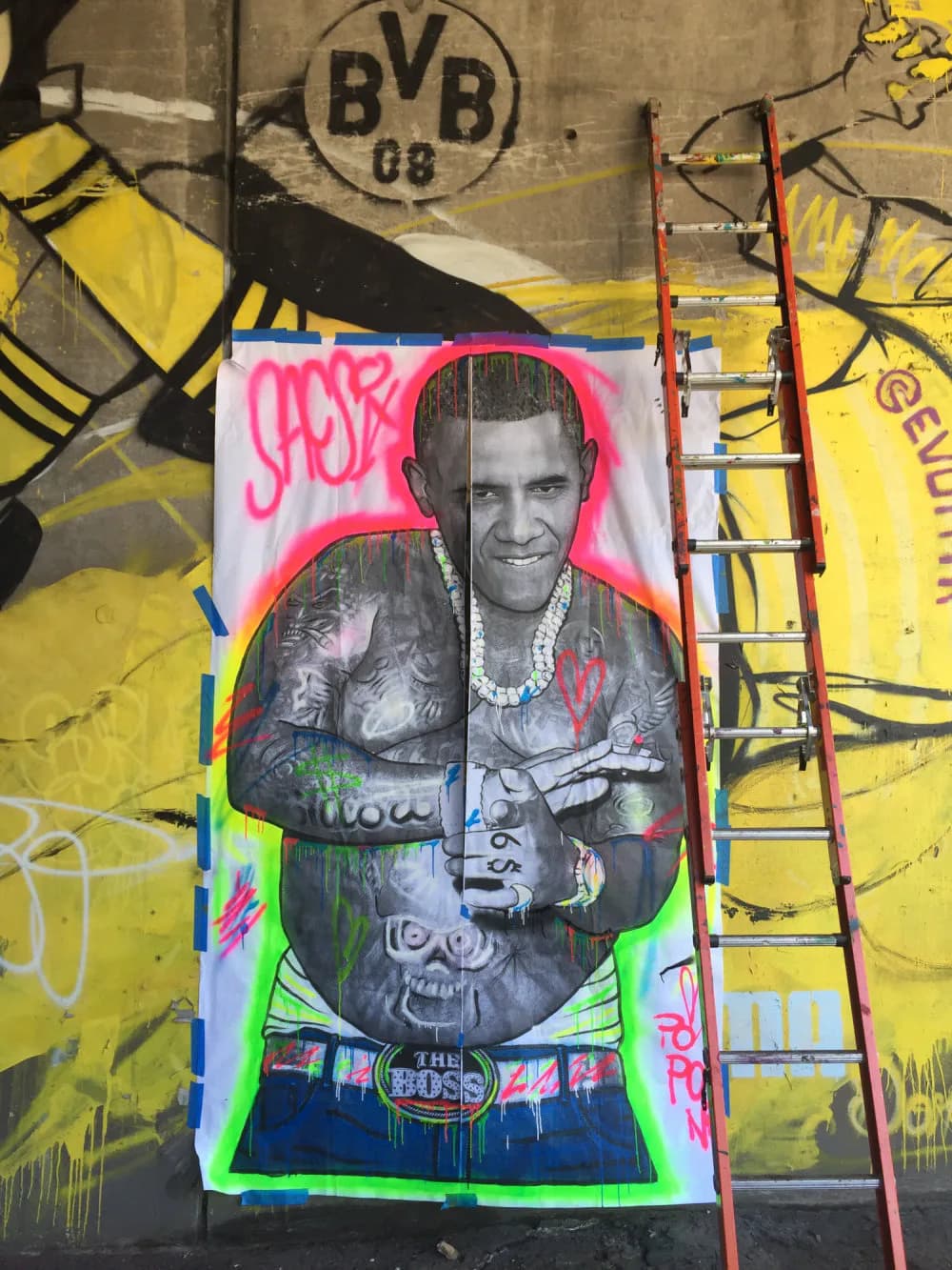 SacSix mural featuring black-and-white portrait with magenta and neon-green outline against yellow background with BVB logo, person holding money.