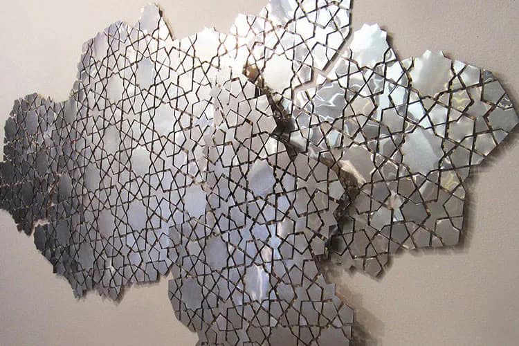 Large-scale wall-mounted installation by Samantha Holmes composed of interlocking geometric wire or mesh forms in varying shades of gray and white, creating an organic, cloud-like silhouette.