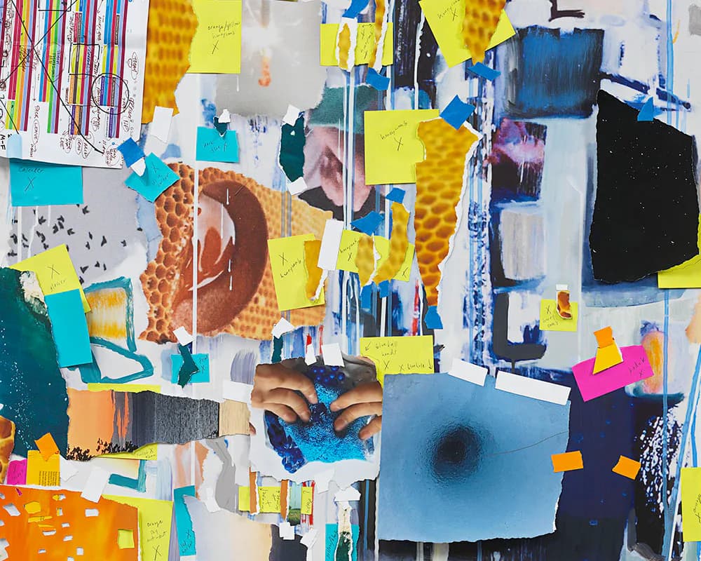 Overhead view of an abstract mixed-media assemblage featuring torn paper, photographs, neon yellow and blue post-its, and hands arranging collaged materials.