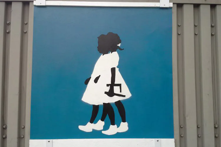 Mural featuring a silhouetted figure with dark skin and white clothing against a bright blue background, holding a stylized black form.