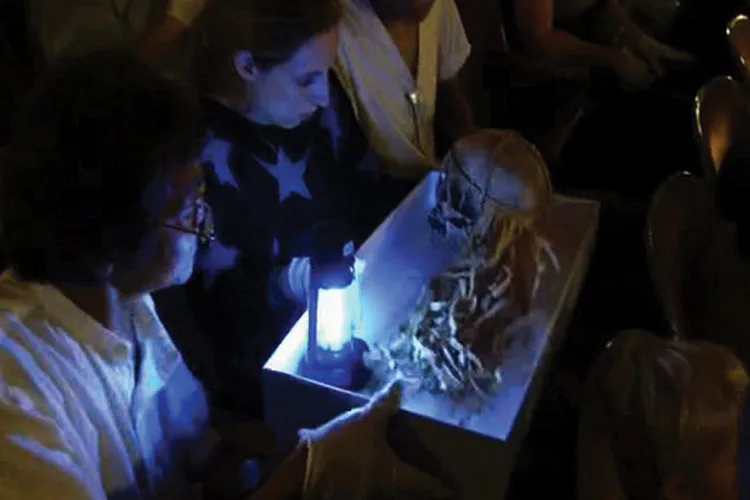 Interactive installation with glowing illuminated surface viewed by visitors in dim lighting; mixed-media piece engaging audience participation.