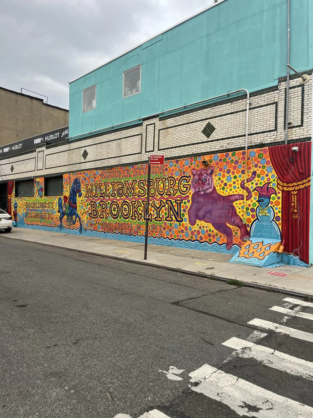 Large mural on building wall reading 'Williamsburg Brooklyn' with vibrant purple, orange, and blue pop-art style illustration and character figures.