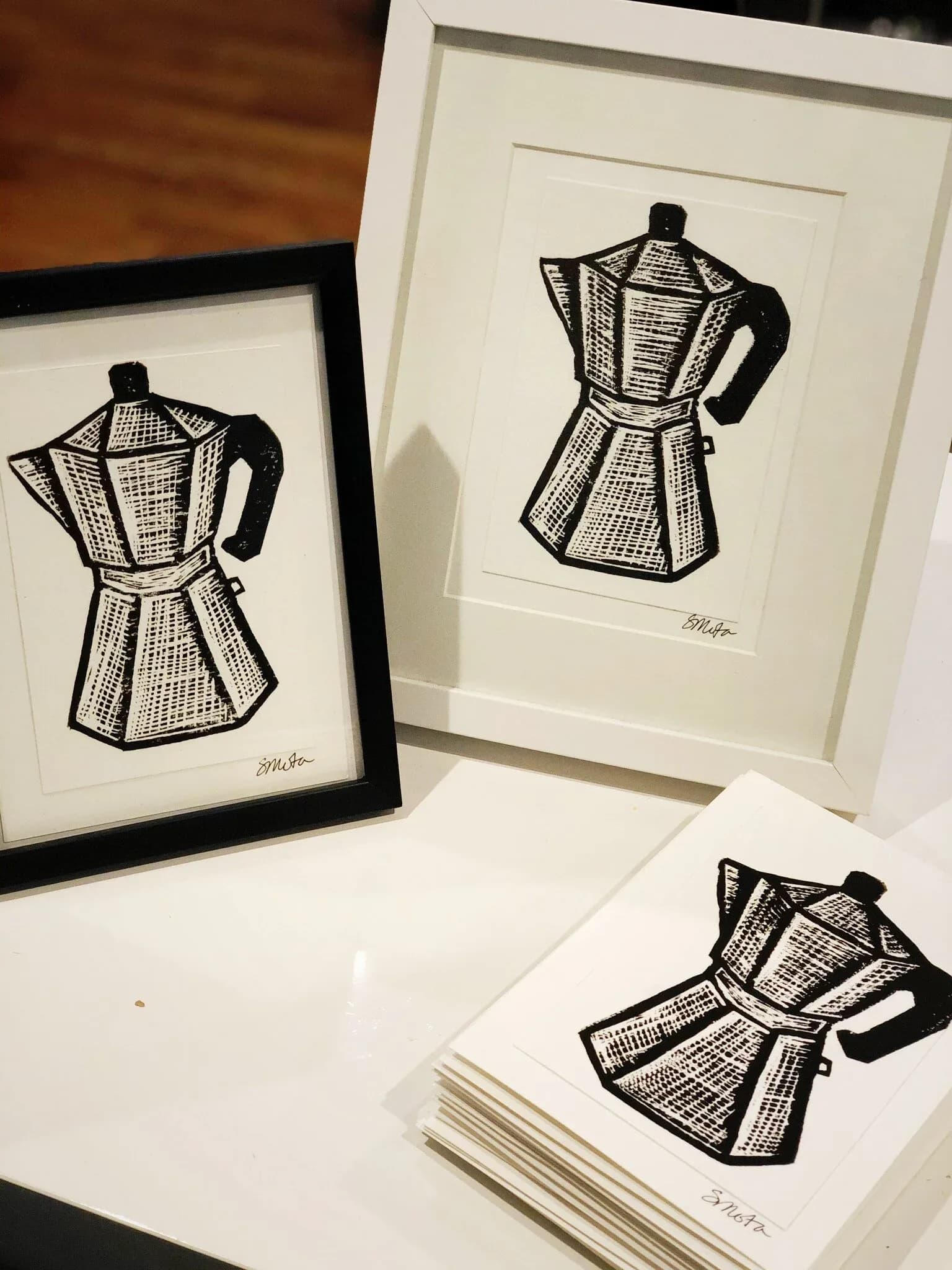 Three black-and-white pen drawings of moka pot coffee makers in varying frame styles: one black frame, one white mat, one loose print.