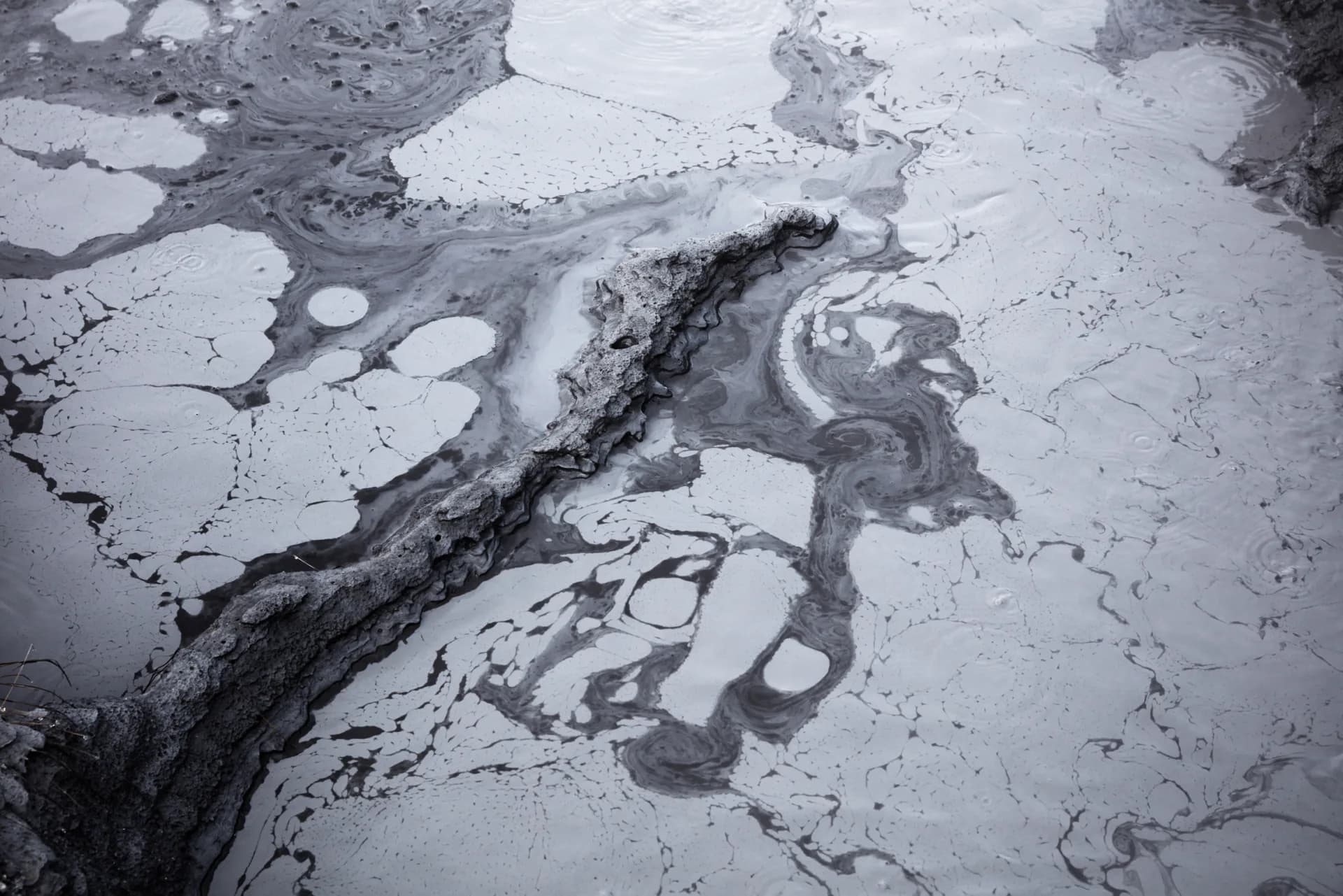 Abstract black and white close-up of swirling ice and dark rock formations on water