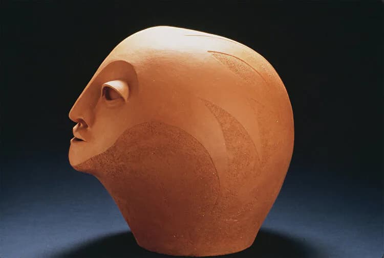 Terracotta ceramic sculpture of an abstracted human head in profile on dark background