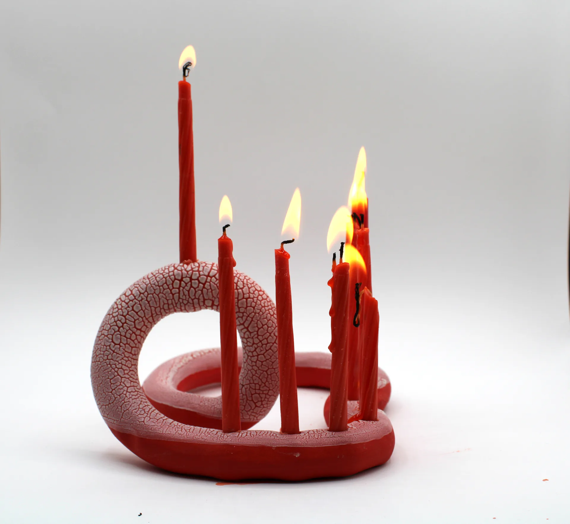 Red snake-form candelabra with partially lit candles, crackle glaze, side view