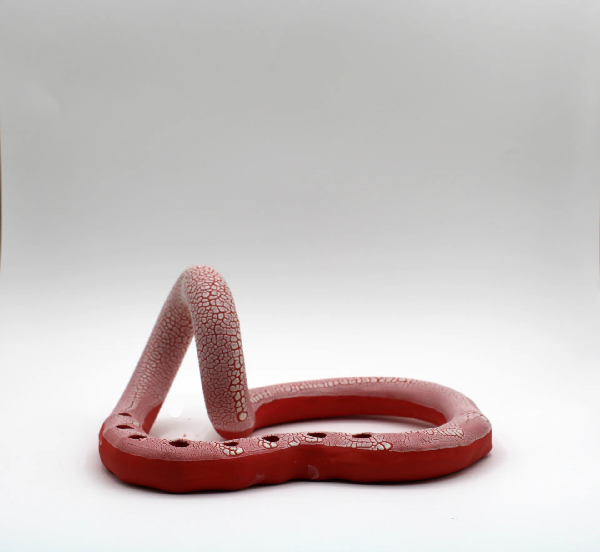 Red ceramic snake-form candelabra without candles, crackle glaze texture, front view