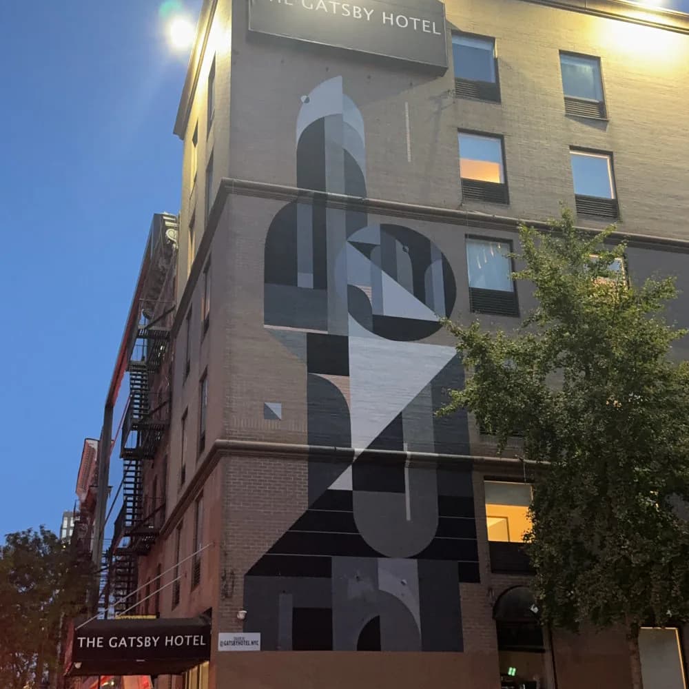 Large-scale mural on The Gatsby Hotel featuring abstract geometric shapes in black, white, and gray tones arranged vertically.