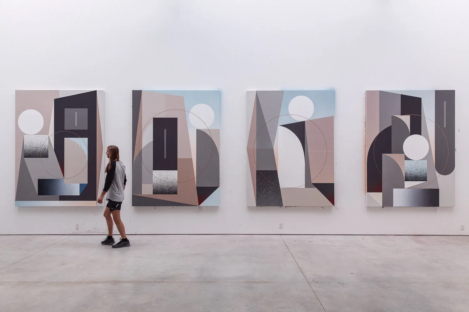 Four large abstract paintings side-by-side featuring geometric shapes in muted pastels, blacks, and whites on white gallery wall.
