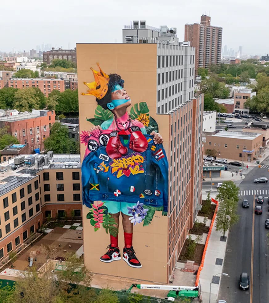 Large-scale building mural depicting a crowned youth with boxing gloves, tropical foliage, and cultural insignia