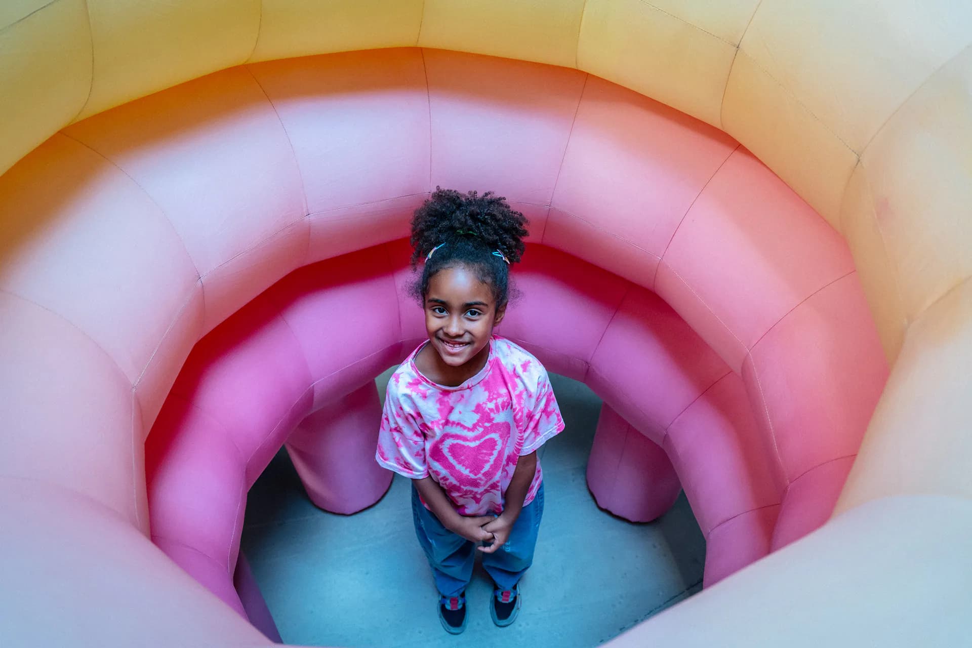Child standing inside a colorful inflatable rainbow arch installation