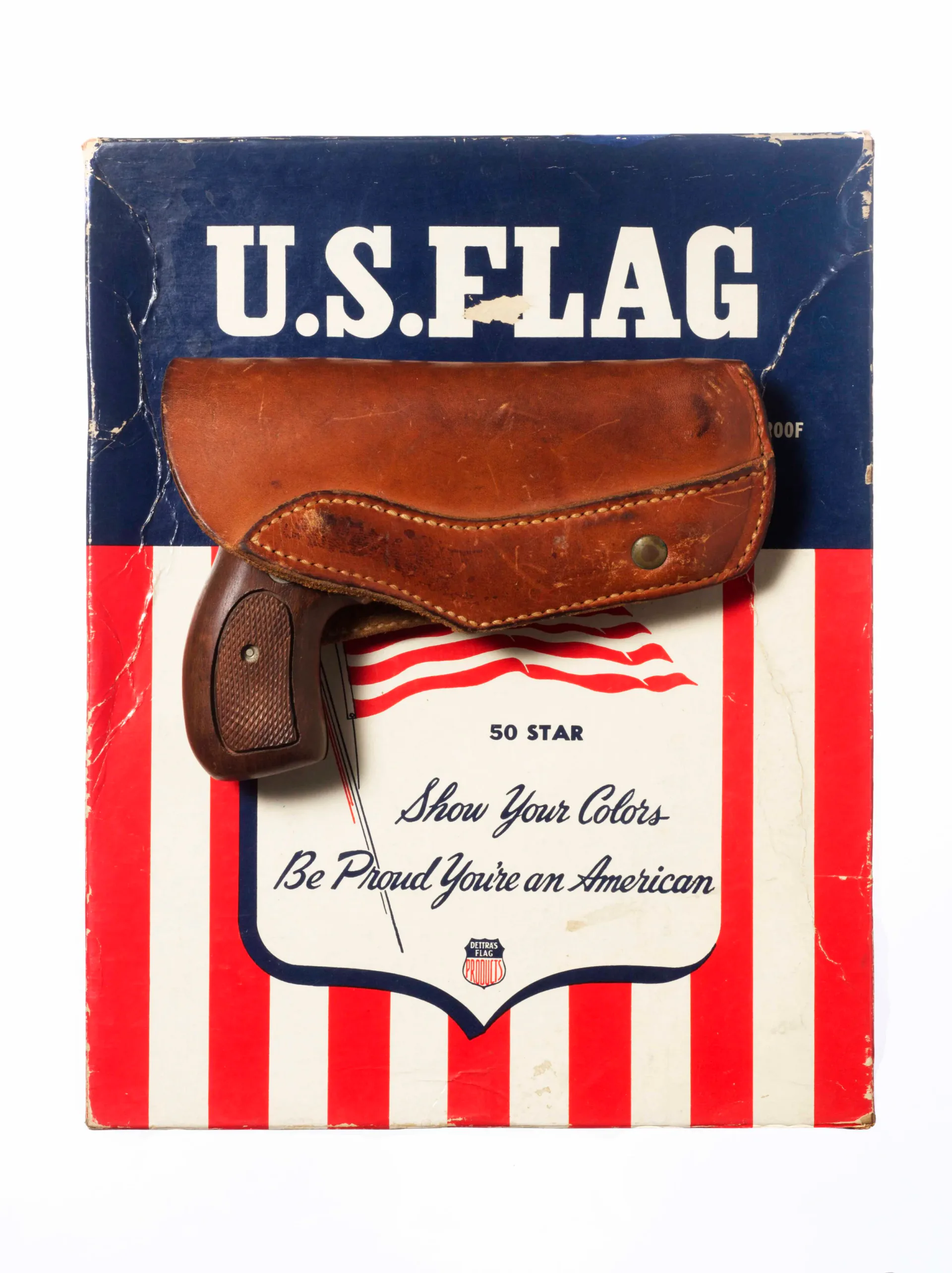 Gun holster resting against a worn U.S. Flag box reading 'Show Your Colors, Be Proud You're an American'