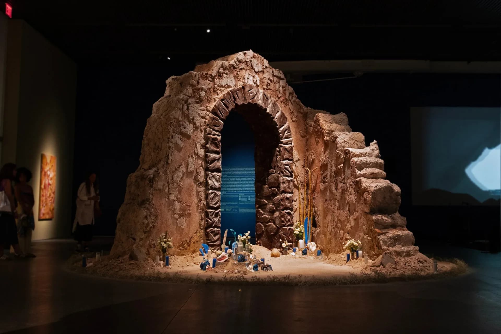 Monumental clay sculptural archway with intricate carved patterns and figures inside, displayed in gallery space.