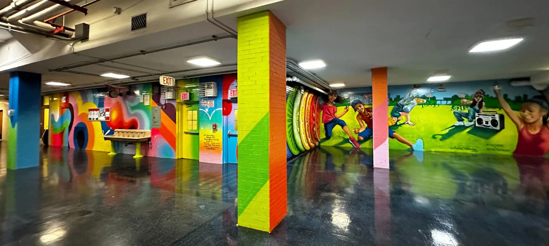 Interior of gallery or creative space with brightly colored columns (blue, yellow, orange) and vibrant abstract murals on walls and floor.