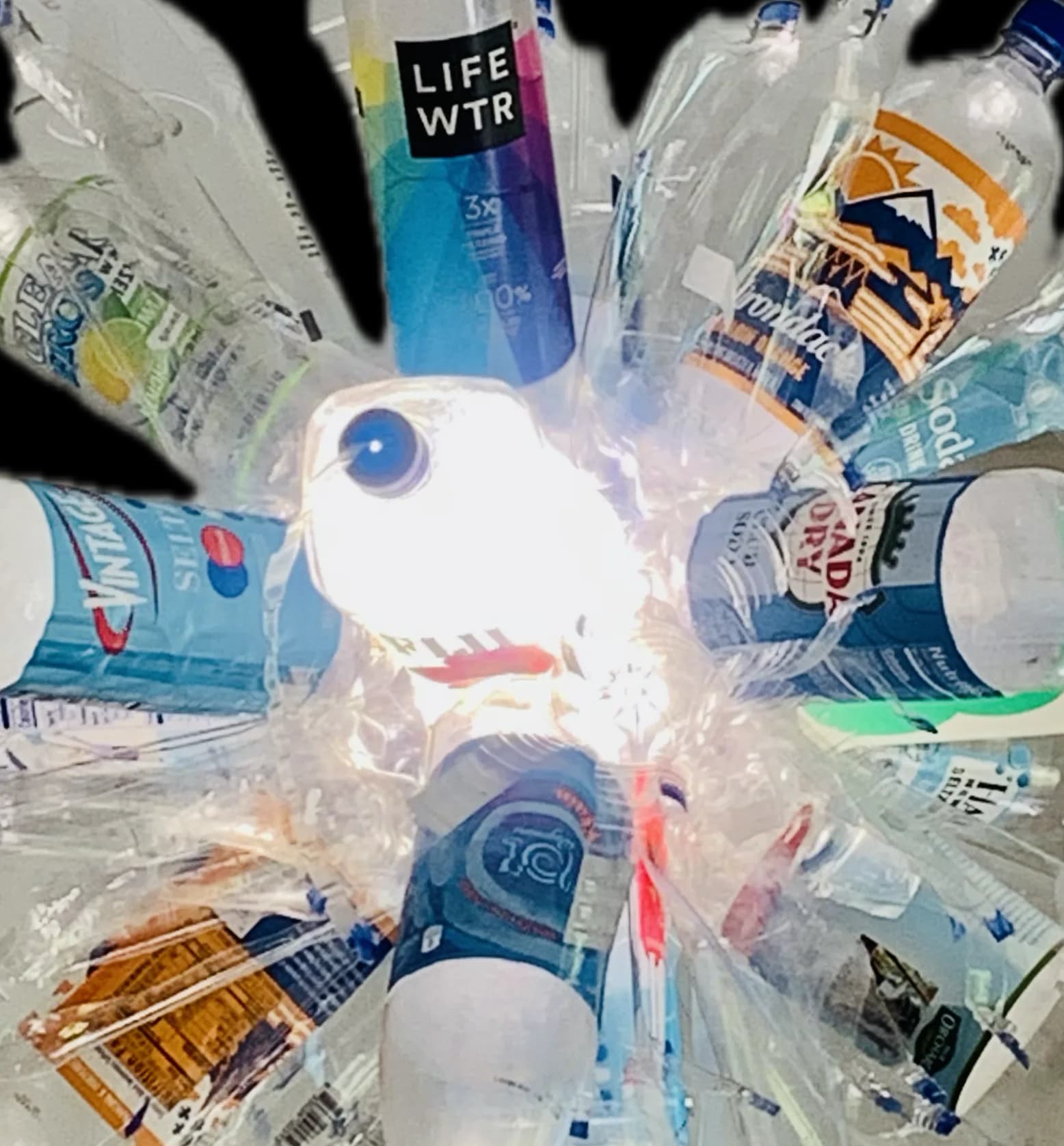 Overhead arranged composition of clear plastic water bottles and beverage containers in a radial pattern around white circular objects.
