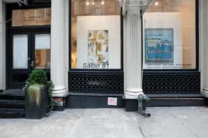 Storefront exterior of Salon 81 gallery with black frame, glass windows displaying artwork, and potted plants outside
