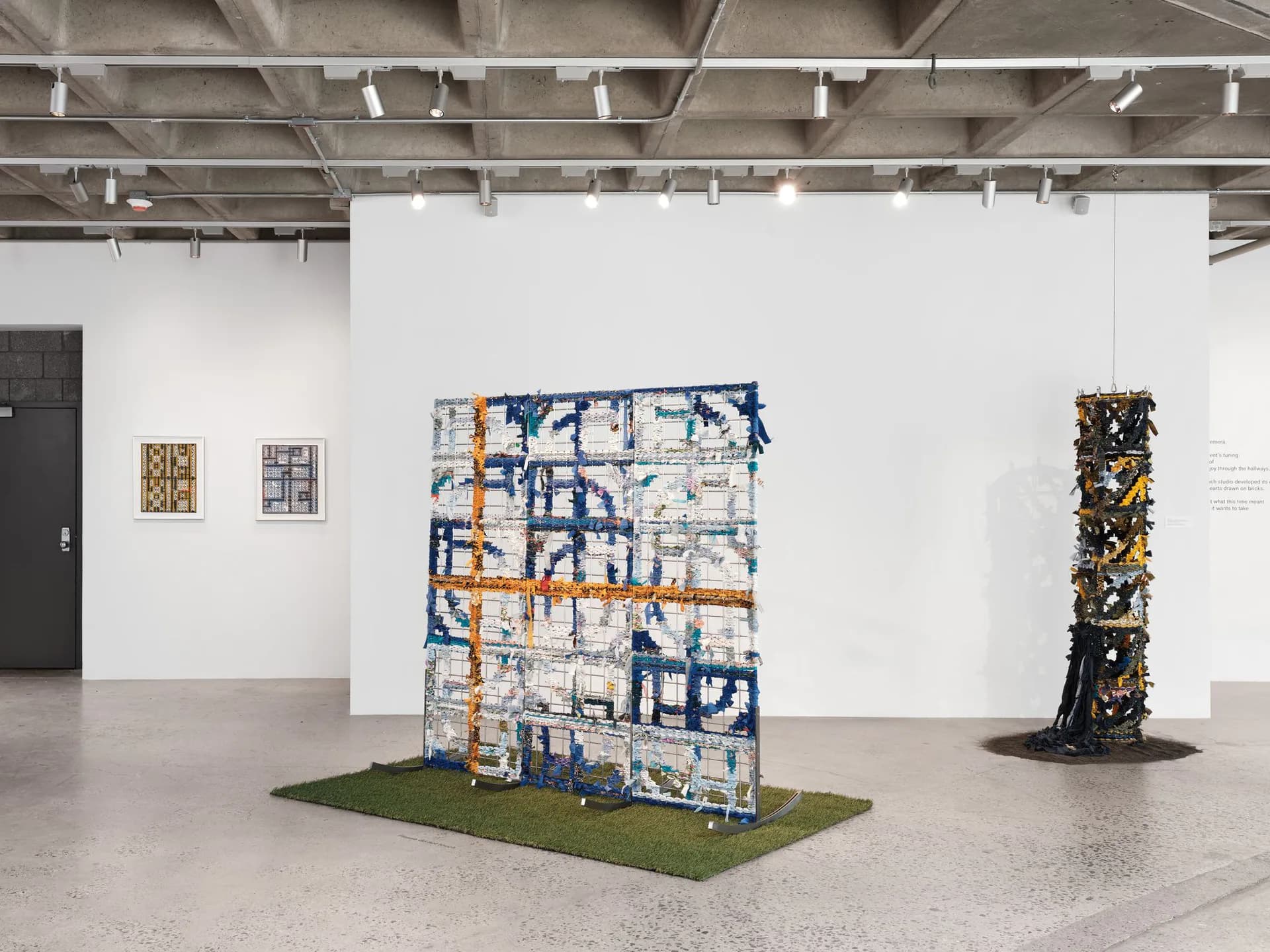 Gallery interior at Abrons Arts Center with white walls, concrete floors, and contemporary mixed-media installations including a blue-and-orange structured artwork on green turf.