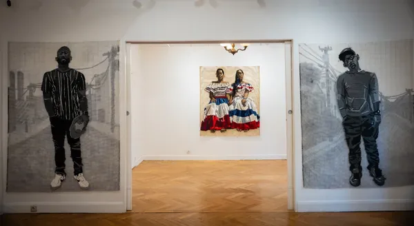 Gallery interior showing two large-scale portrait drawings on side walls flanking a central doorway with embroidered artwork visible inside.