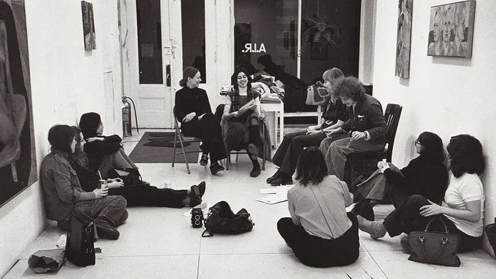 A.I.R. Gallery interior with seated participants arranged in a circle on a white floor during a community gathering or workshop.
