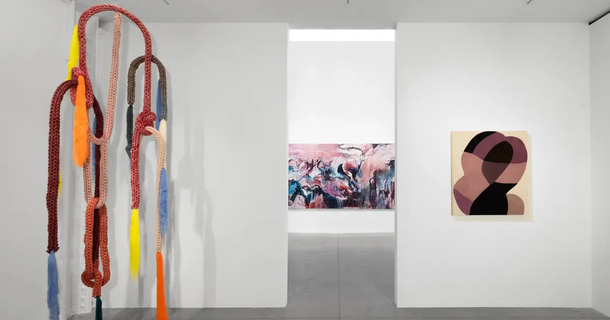 Gallery interior with colorful coiled rope sculpture on left wall, centered photograph, and abstract artwork on right wall.