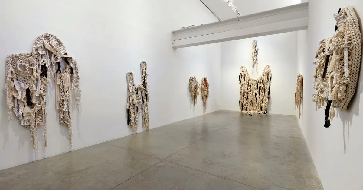 Gallery interior displaying textile sculptures with organic, draping forms in neutral and metallic tones mounted on walls.