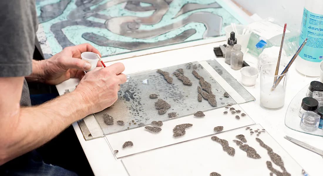 Hands examining preserved specimens and archaeological artifacts laid out on a white work surface in a studio setting with tools and containers nearby.