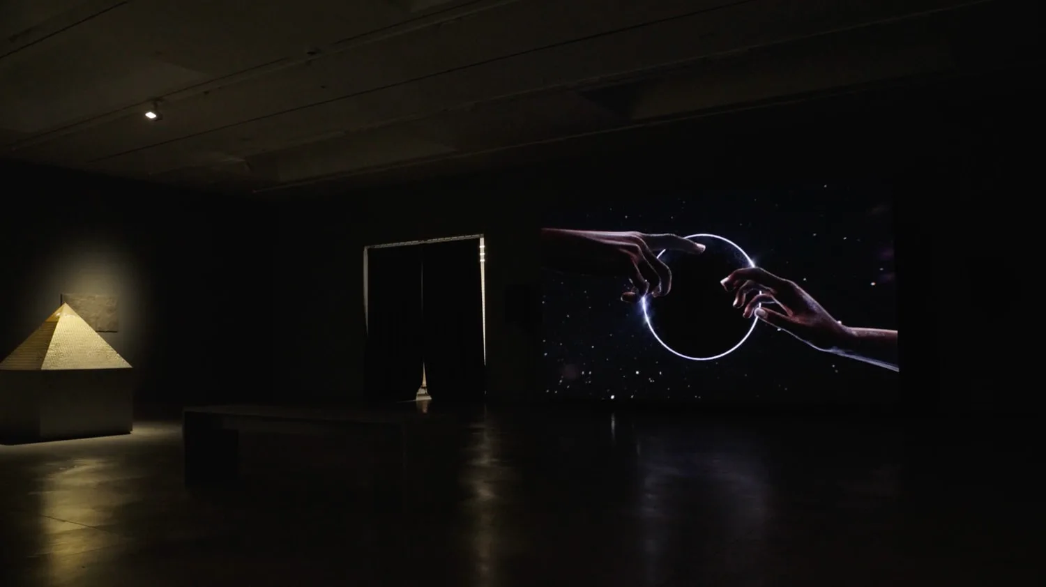 Dark gallery installation with neon blue and purple circular light sculpture on right, geometric frame structure center, and golden triangular light form on left wall.