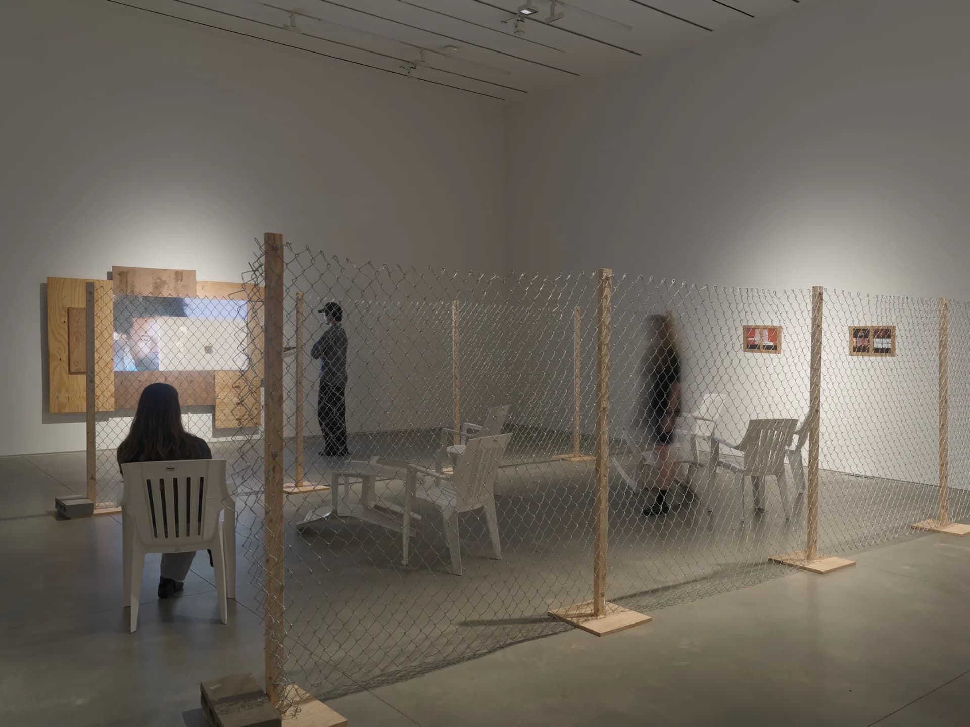 Gallery interior with mesh enclosures containing chairs and figures, wooden structural elements, white walls, and overhead lighting at Amant.