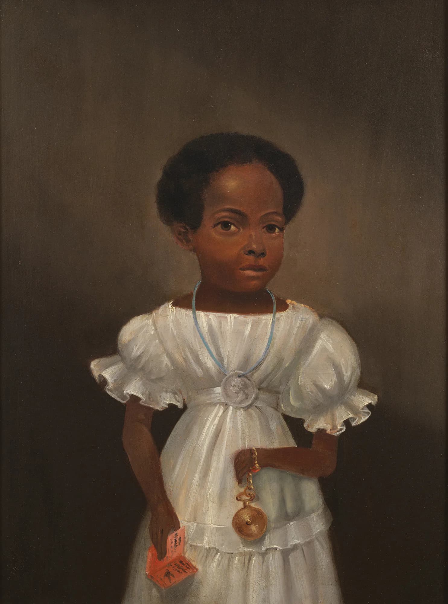 Portrait of a young Black child wearing a white off-shoulder dress with blue trim and holding an orange toy against a dark neutral background.