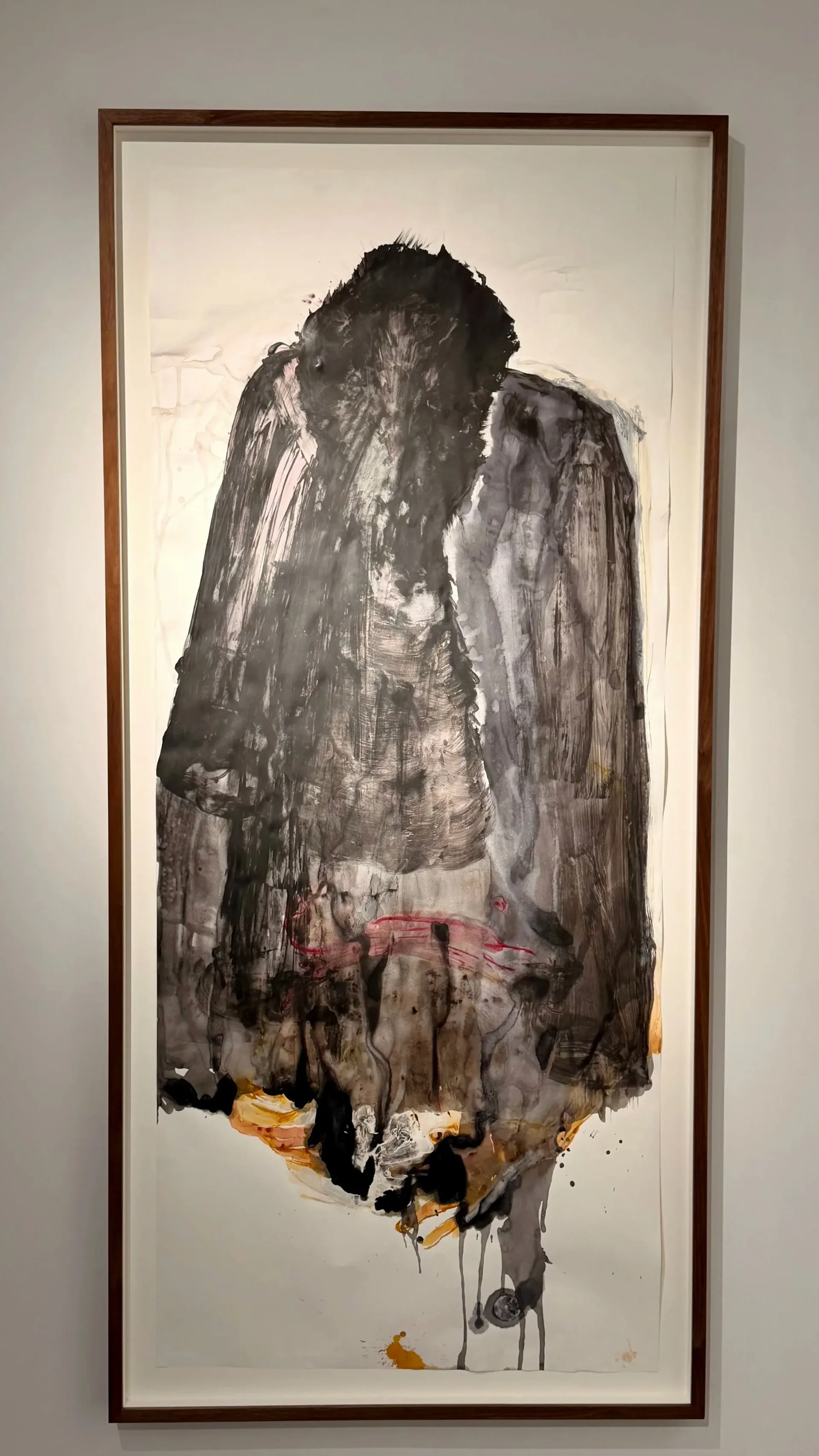 Abstract mixed-media figure rendered in charcoal, ink, and gold pigment on paper; dark gestural marks form a hooded form with hints of pink and orange at base.