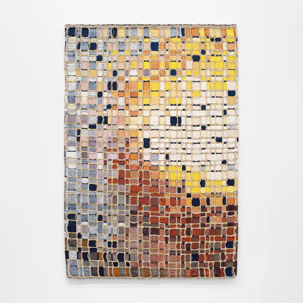 Abstract textile or woven wall piece with a gradient of small colored squares transitioning from pale yellows and blues at top to deep reds and oranges at bottom.