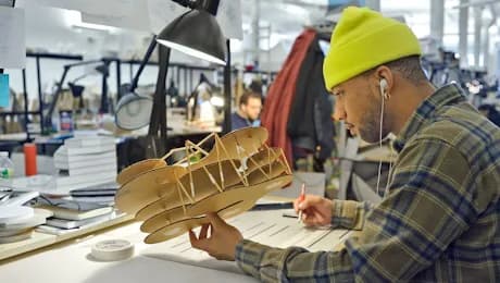 Wooden sculptural model of an airplane or aircraft, displayed on a work surface with studio environment in background.
