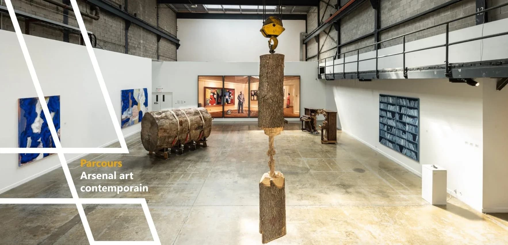 Arsenal Contemporary gallery space with wooden sculptural forms suspended from ceiling, concrete floors, industrial skylights, and framed artworks on walls.