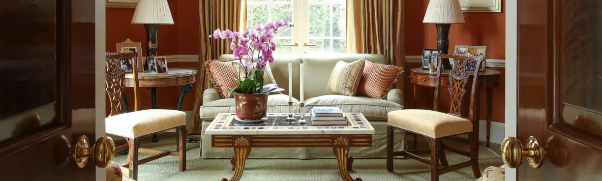 Elegant Art Peritus sitting room with a cream sofa, patterned armchairs, a floral centerpiece, and antique wooden furniture on a green carpet