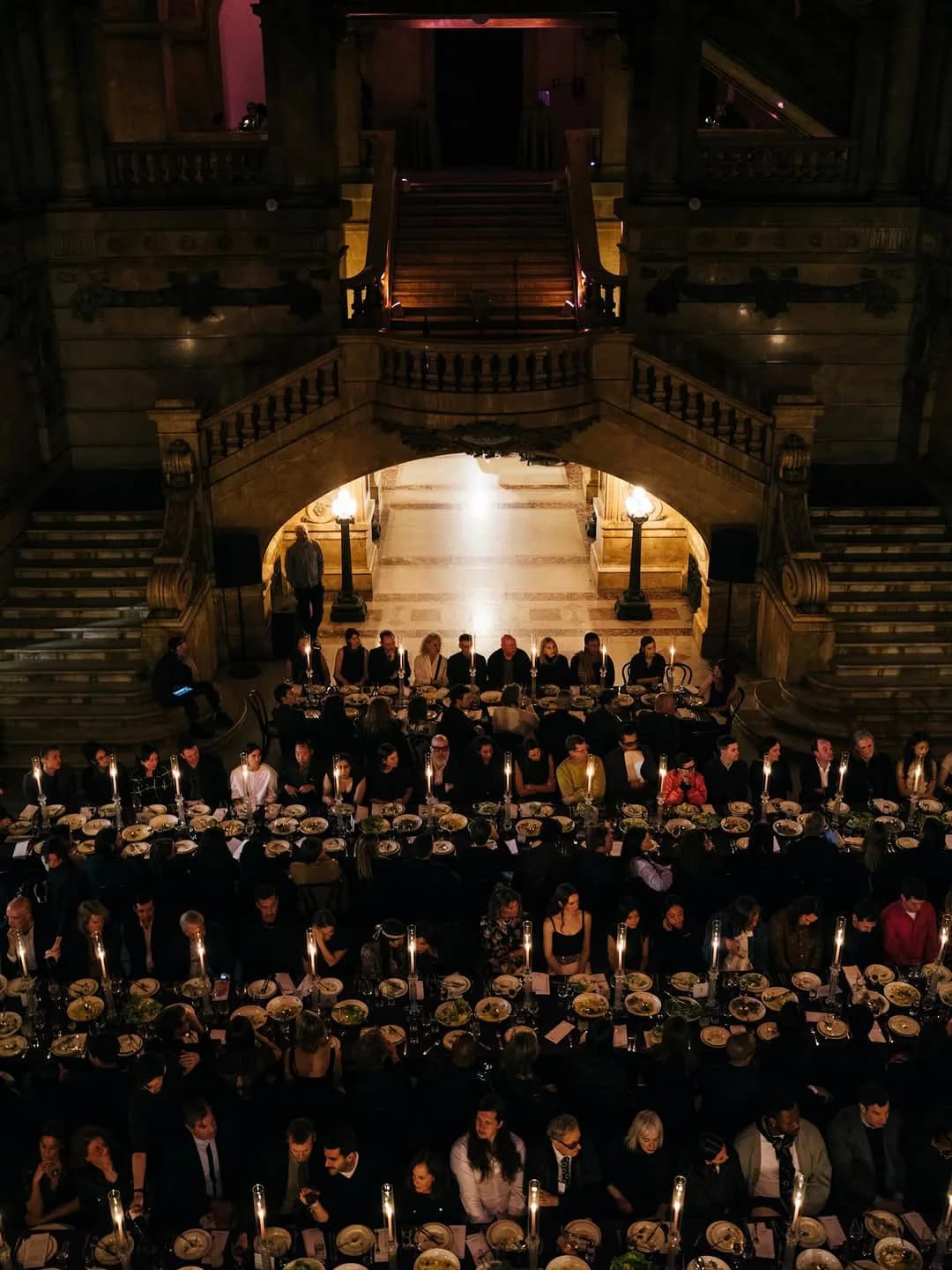 Interior photograph of grand classical hall with ornate balconies, arched ceiling, warm lighting, and formal gathering of people in evening attire.