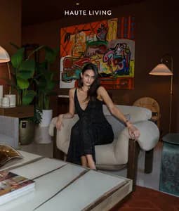 Haute Living gallery space with woman on cream seating, bold colorful abstract painting, pendant lamps, and contemporary furnishings.