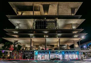 Modern multi-level gallery building exterior at night with illuminated windows, colorful artwork displays, and ground-level entrance.