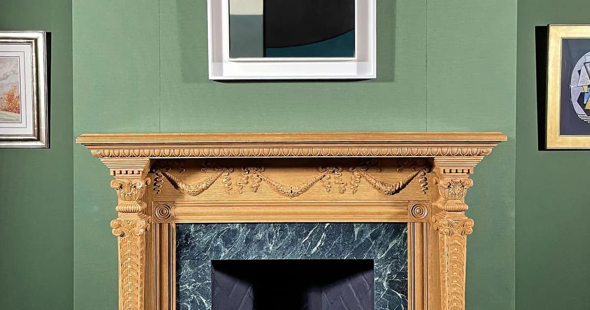 Gallery wall painted green with a carved wooden fireplace mantel and framed artworks displayed above and beside it