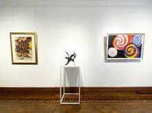 Gallery wall at Barbara Mathes Gallery with two framed artworks flanking a sculptural figure installation on wooden floor.