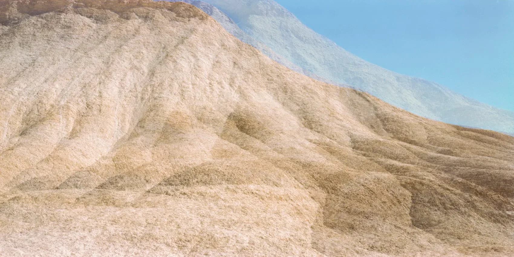 Photograph of eroded white and tan hillside with deep gullies and ridges, clear blue sky, depicting desert geological formations.