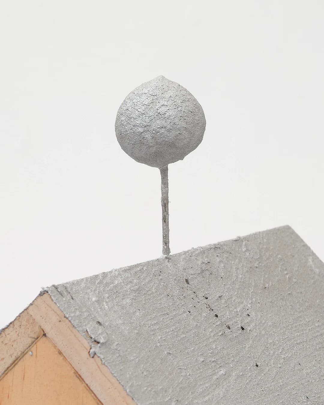Concrete sphere balanced on a thin stem, mounted on a textured gray platform with beige wooden trim.