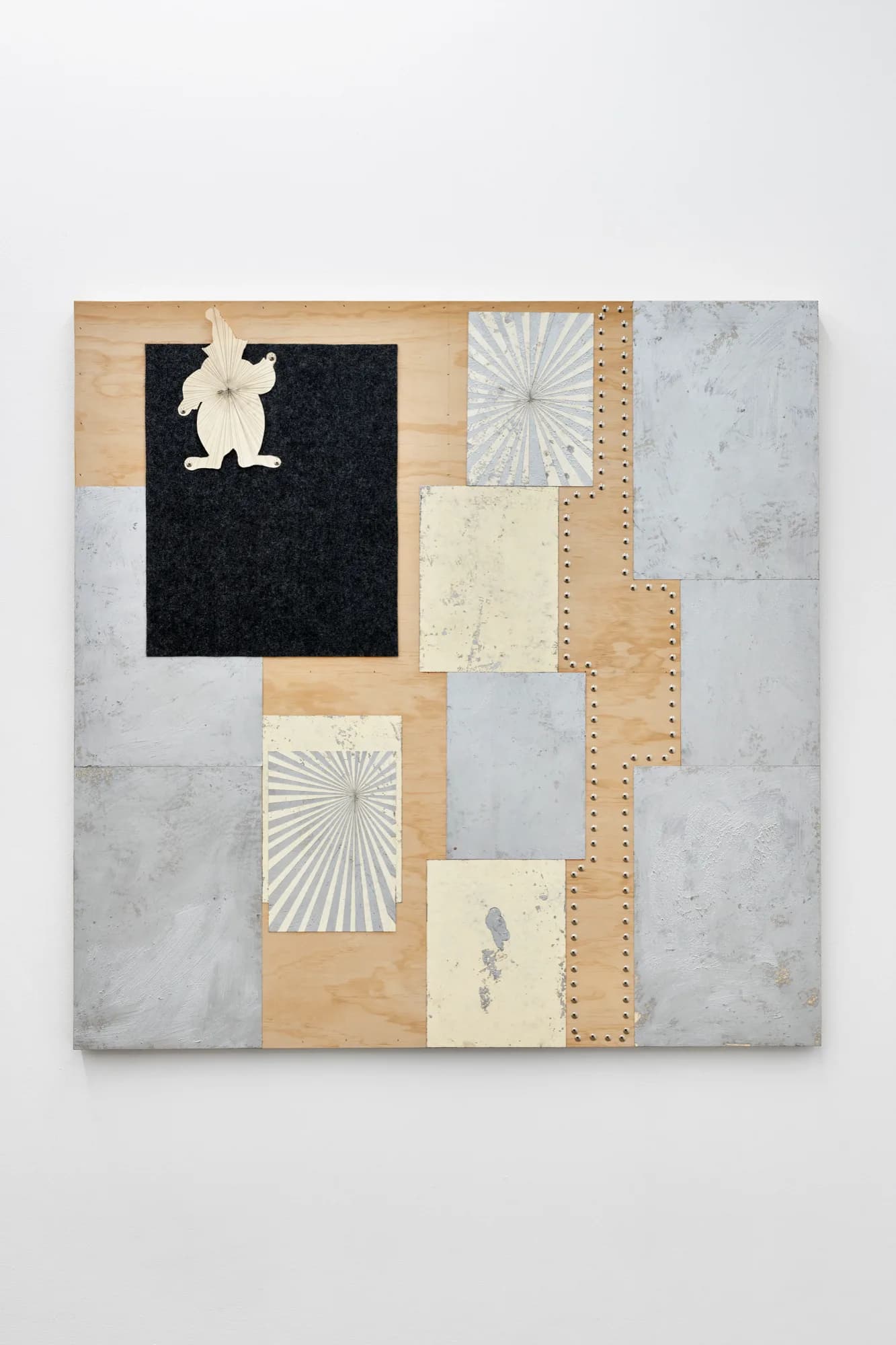Mixed-media collage on wood featuring patchwork of marble, wood, black felt, cream paper, and botanical prints arranged in geometric grid with a white sculptural form at top.