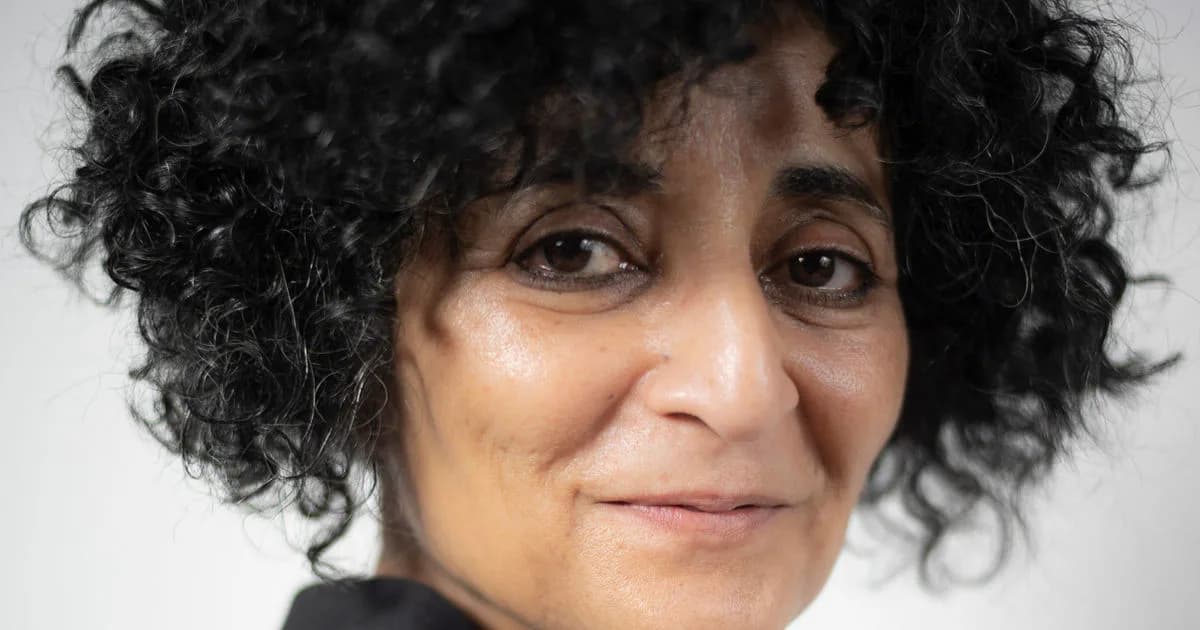 Close-up portrait of a person with curly dark hair and warm expression against a light gray background.