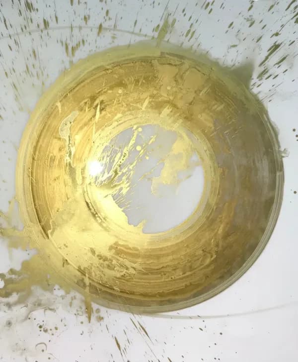 Abstract circular form with gold and yellow metallic paint strokes on white and speckled background, creating dimensional spiral composition.