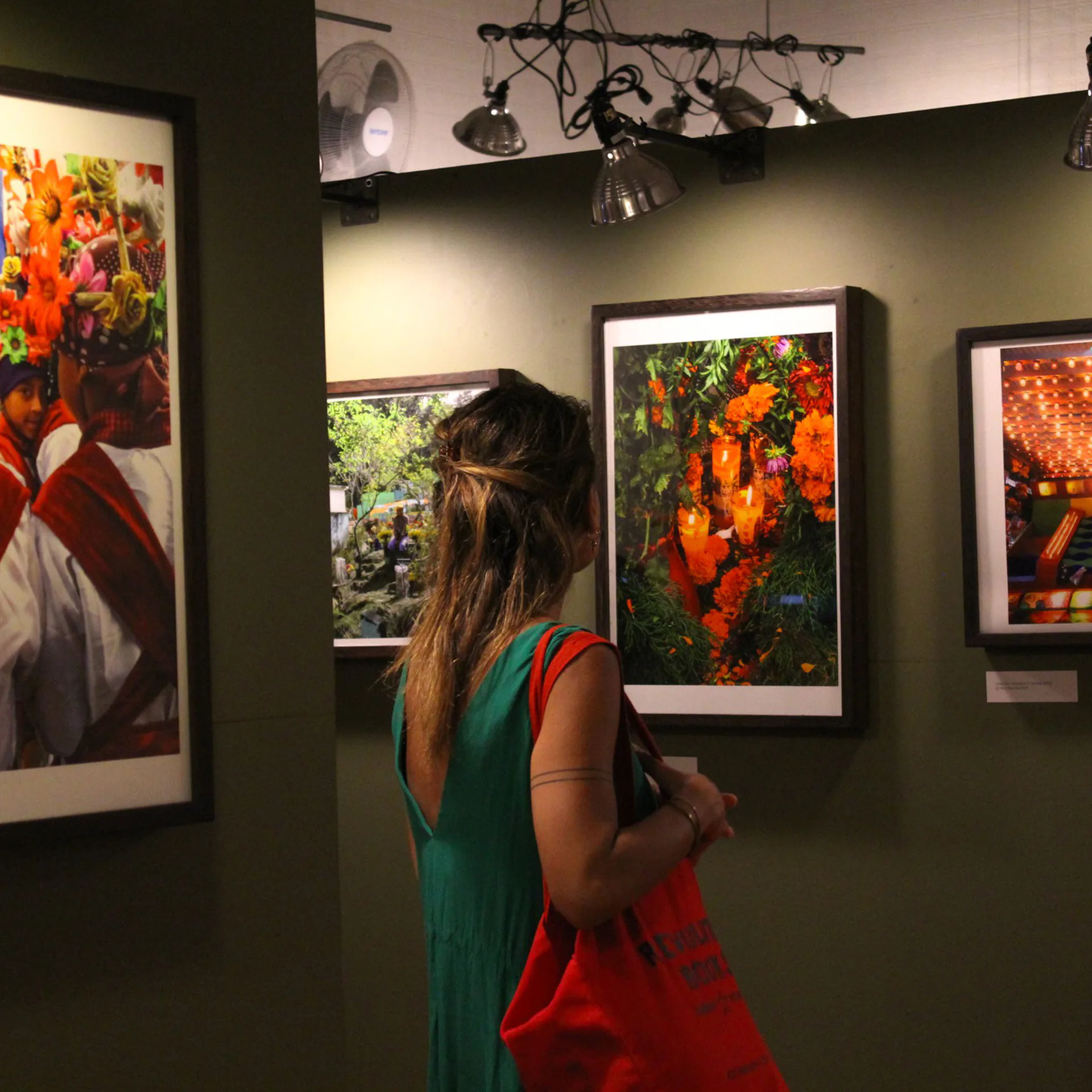 Woman in a green dress views framed color photographs on a gallery wall, one showing marigold flowers, in the Bronx Documentary Center