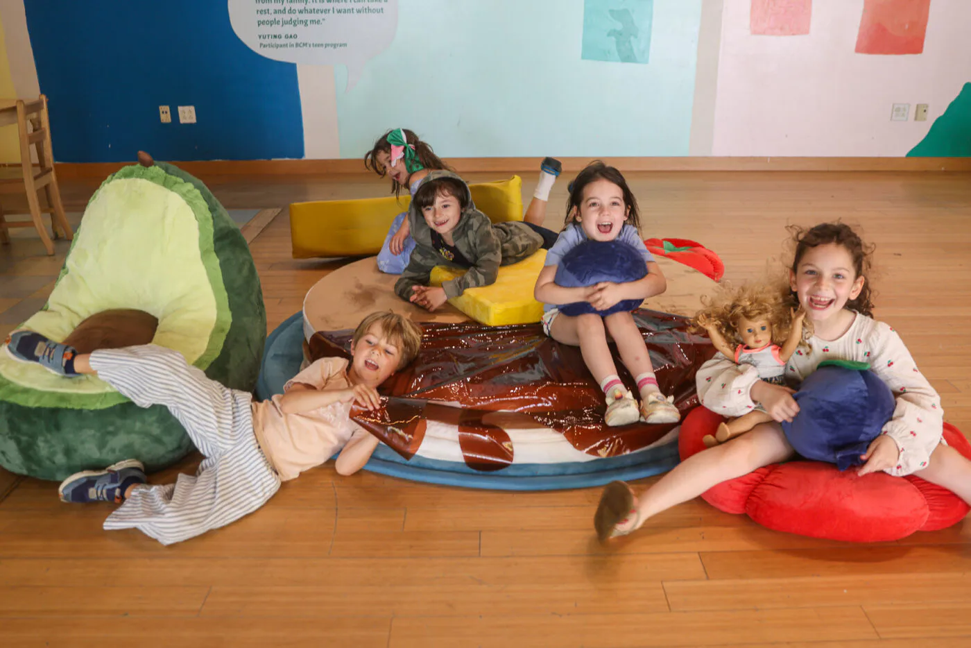 Children playing on colorful mats and cushions on a wooden floor in Brooklyn Children's Museum with green and yellow structures.