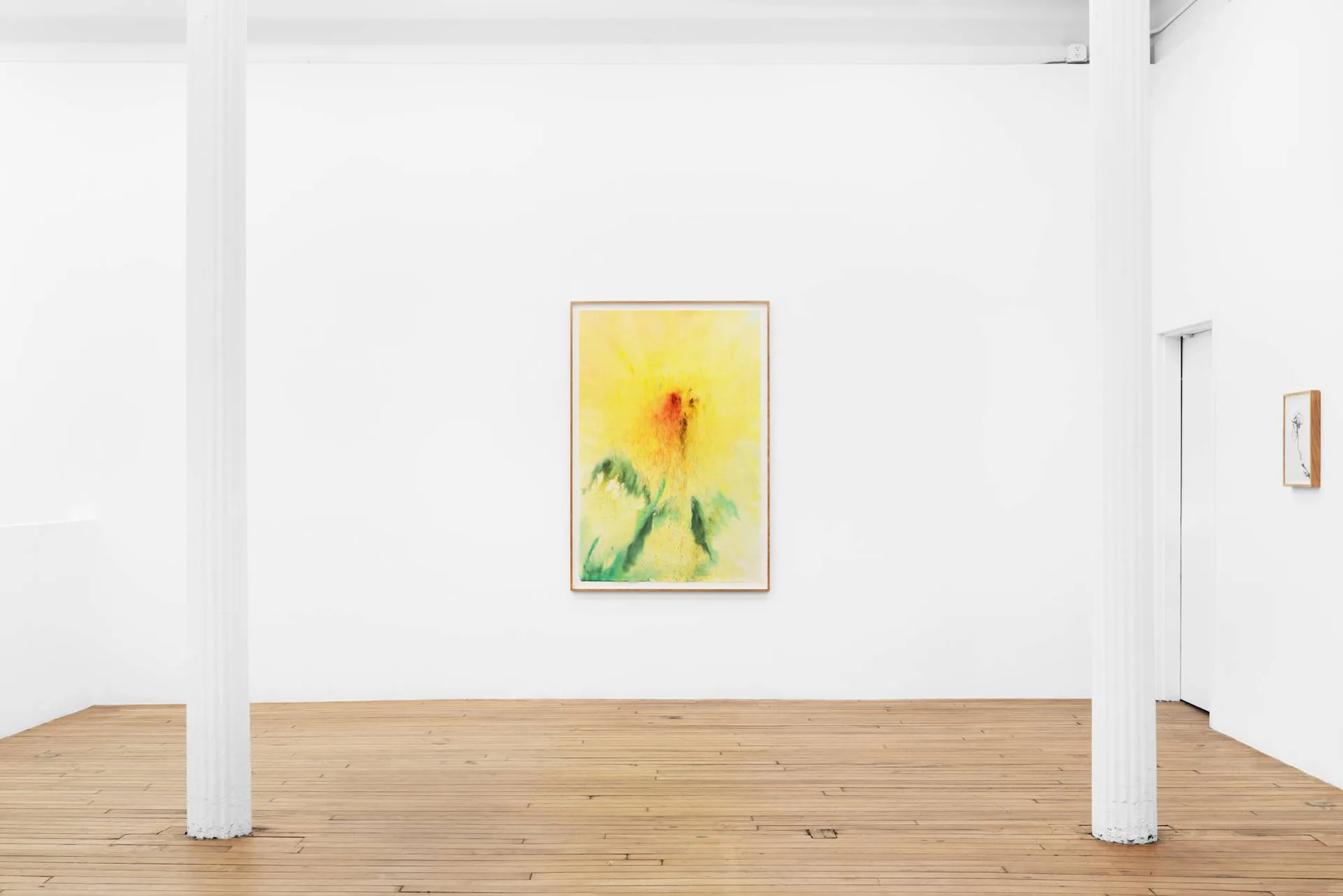 Gallery interior with white columns, wooden floor, and a small framed yellow floral artwork hanging on white wall.
