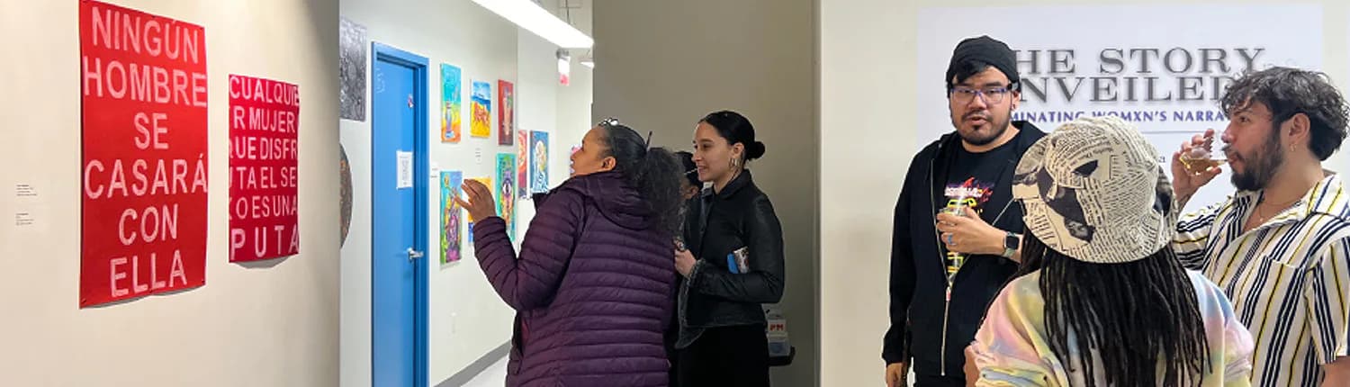 Gallery visitors viewing wall-mounted artwork and text panels in white interior space, one person holds large circular artwork.
