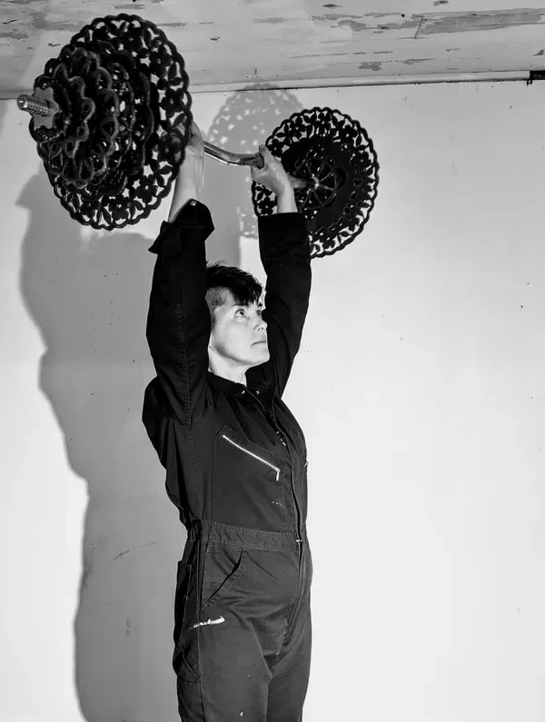 Black and white portrait of a person in dark clothing holding two large circular sculptural wire forms overhead.